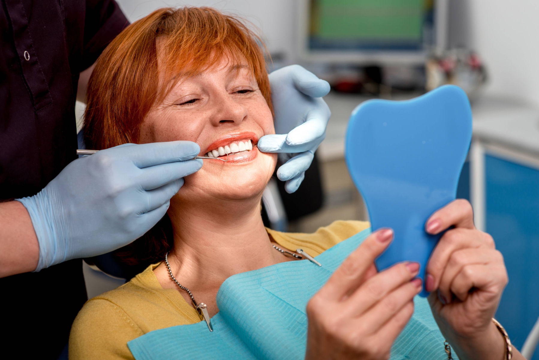 A smiling woman looking at her cosmetic dentistry results in the mirror