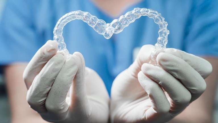 A dentist holding Invisalign trays in the shape of a heart
